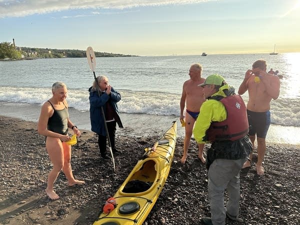 A group gathers around a kayak on the beach.