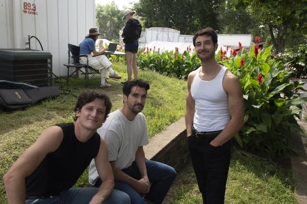 Three guys relax behind a performance space at a fair