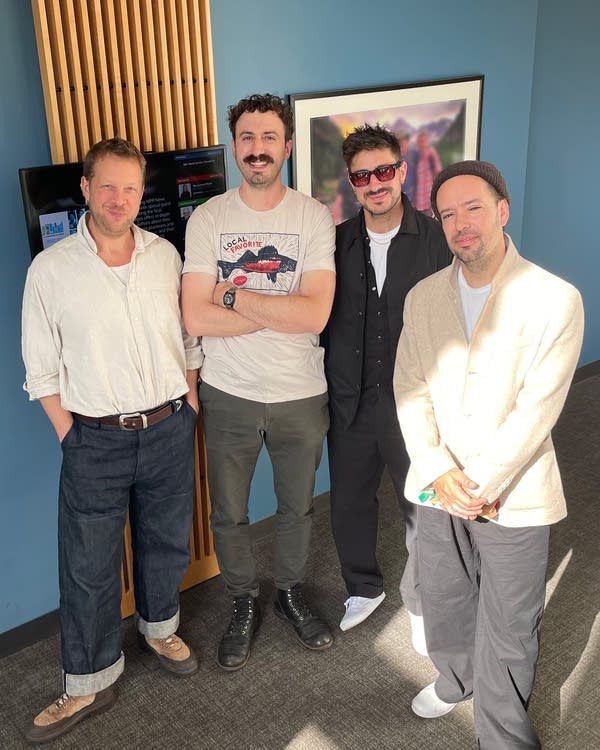 Four men stand together in a sunny atrium for a group photo