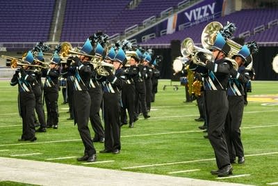 A marching band performs on the field of a football stadium.