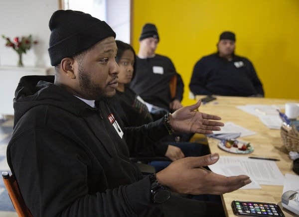 A man gestures while sitting on a conference table. 