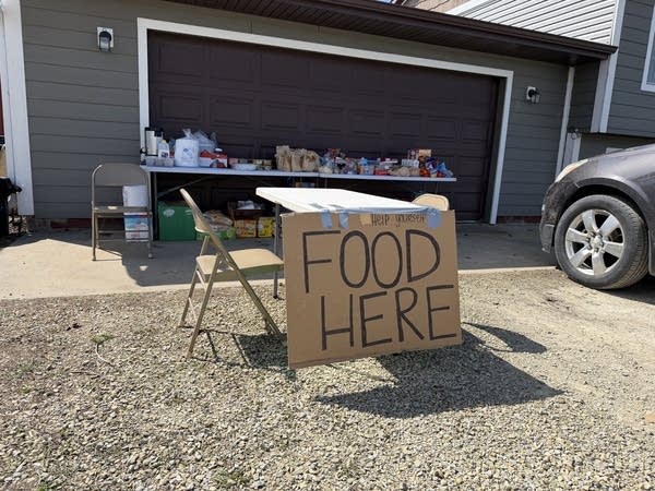 A table in a driveway is filled with food with a cardboard sign reading "FOOD HERE" in front.