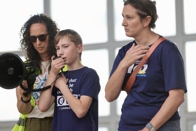 A boy speaks into a bullhorn with women standing at his sides.
