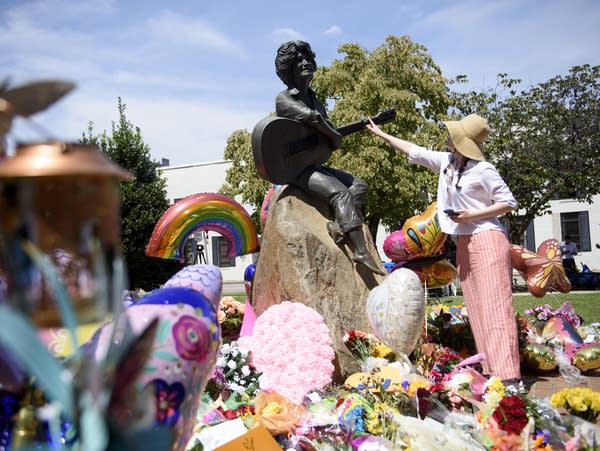 People place balloons and flowers near a statue of Dolly Parton.