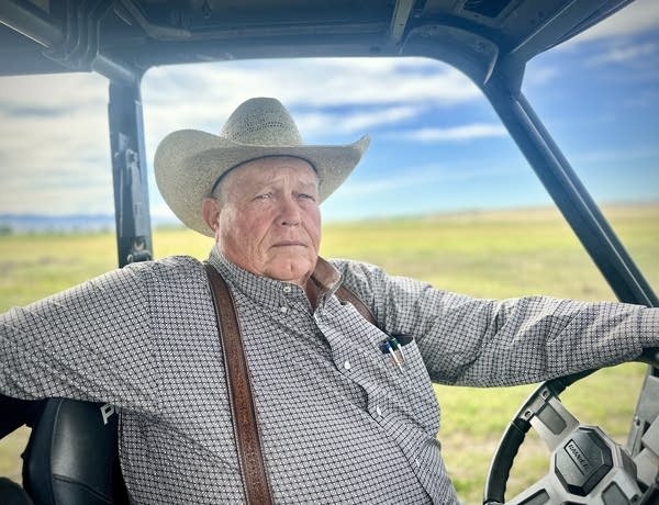 A man in a cowboy hat sitting in an ATV with green grass behind him.