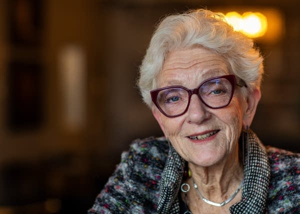 A woman with white hair and glasses sits for a portrait