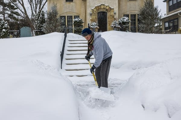 A man shovels snow from the sidewalk.