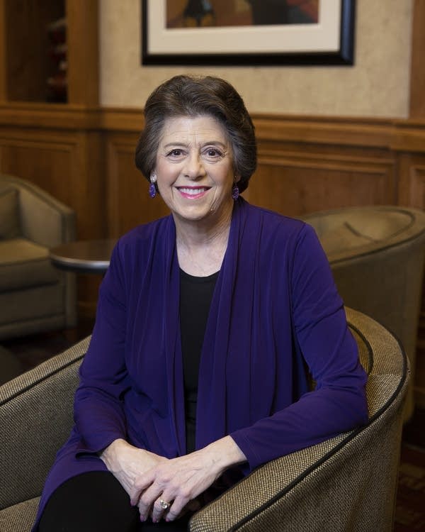 A woman wearing a purple cardigan sitting on a chair.