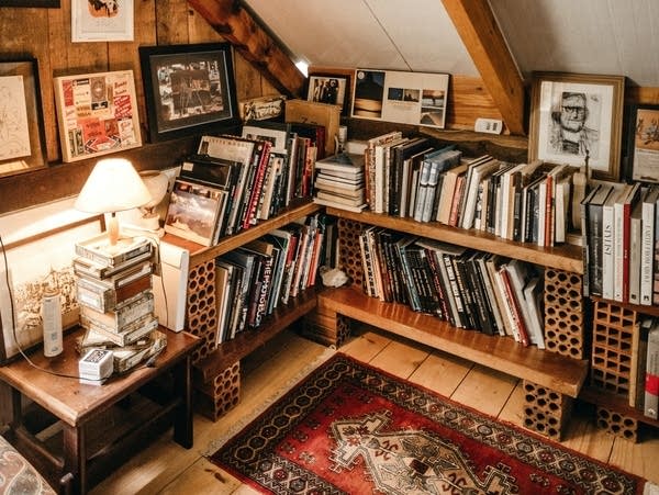 A full bookshelf with lots of art hanging above it.