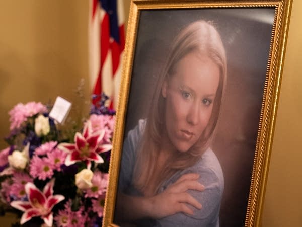 A portrait of a woman sits next to flowers.