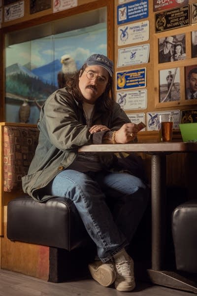 Dan Hornsby wears a baseball cap and barn jacket. He is sitting in a booth.