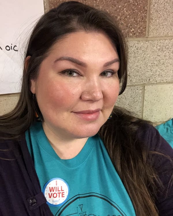 A woman poses for a portrait wearing an "I Will Vote" sticker.