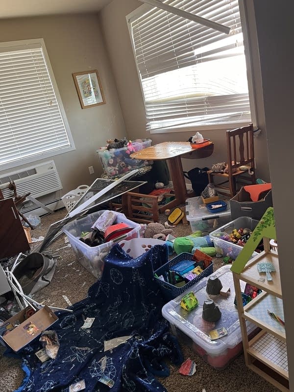 A room in an apartment with a broken window and belongings spread around.