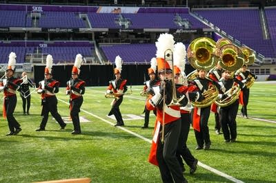 A marching band performs on the field of a football stadium.