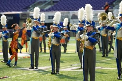 A marching band performs on the field of a football stadium.