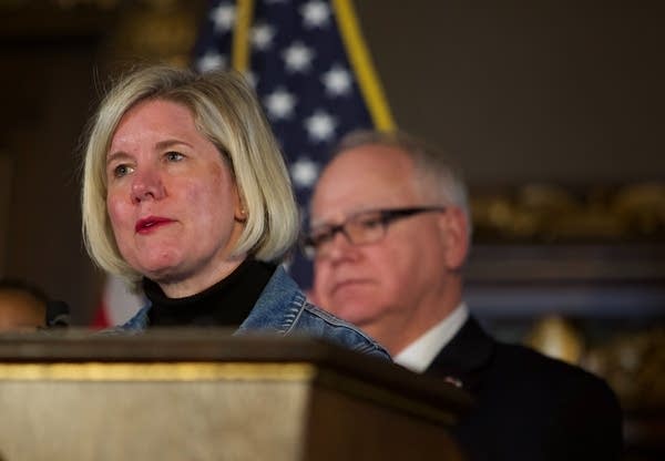 A woman stands at a podium with a man behind her.