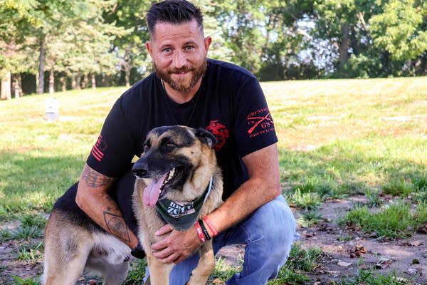 A man poses for a photo while kneeling down with his German shepherd.