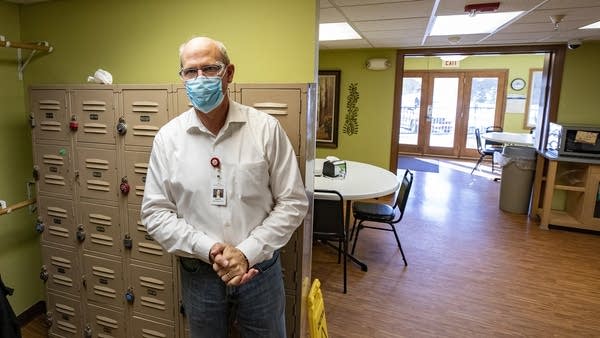 A man wearing a face mask stands in a break room. 