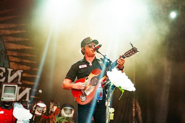 A musician sings and plays guitar on an outdoor stage