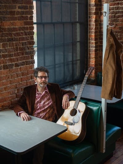 A man sitting in a booth in a cafe, next to his guitar