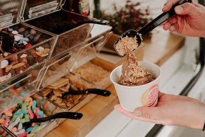 A person scoops a topping onto a swirl of frozen yogurt.