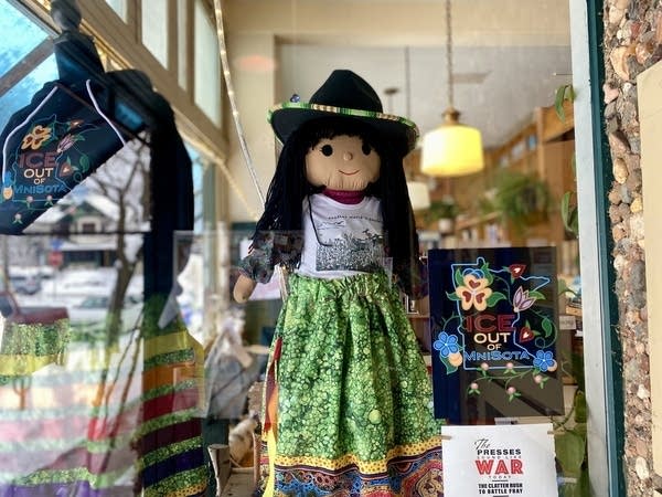 A doll stands on display with a poster and a tshirt.