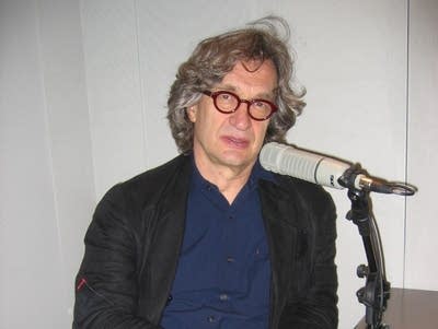 A man in glasses sits at a microphone in an edit suite