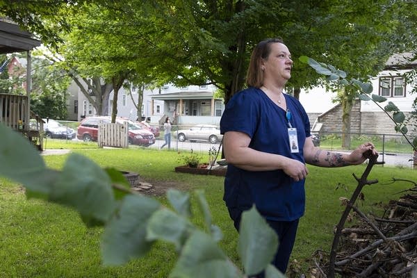 A woman wearing scrubs stands in the front yard of a house.