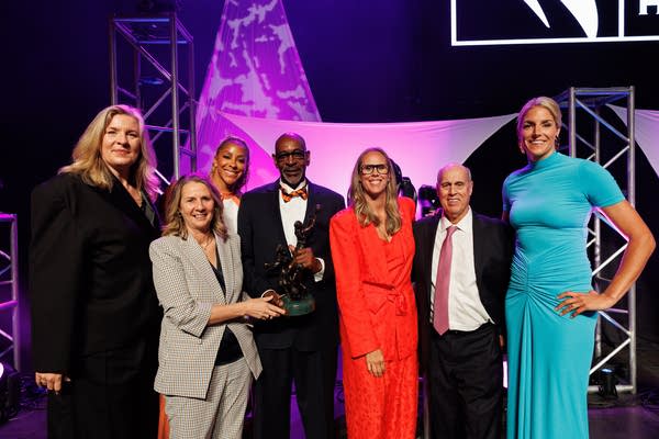 A group poses for a photo on a stage lit in purple.