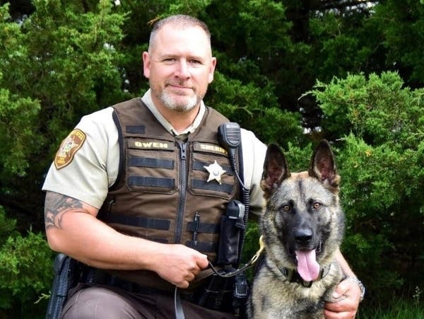 A police officer kneels next to a canine.