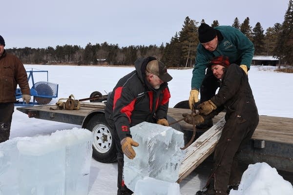 People load a large block of ice onto a truck bed.