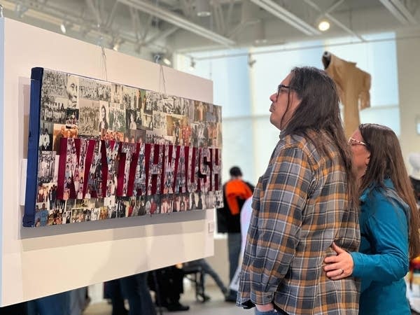Two people look at a canvas on a wall in an art exhibition. 