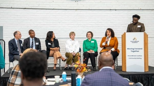 People sitting on a stage listen to someone talking