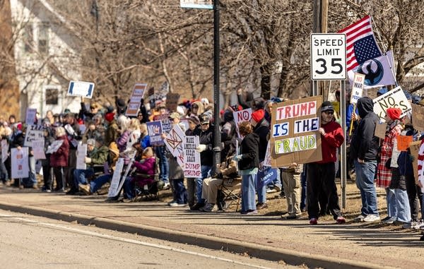 People hold signs on the sidewalk