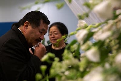 A man wipes his face with a handkerchief while looking into a casket