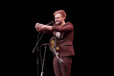 A musician sings and gestures onstage in a music venue
