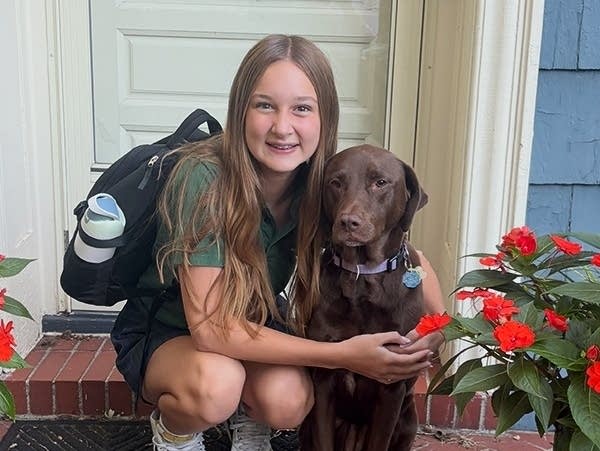A girl kneels down to hug a dog.