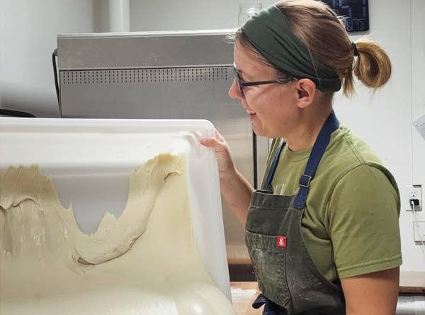 A baker pours dough out of a plastic tub.