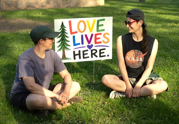 Two people sitting outside by Love Lives Here sign