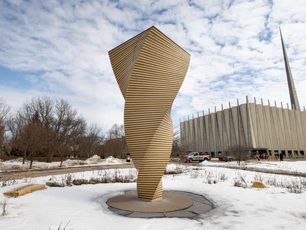 A spiraling sculpture stands in front of a chapel building