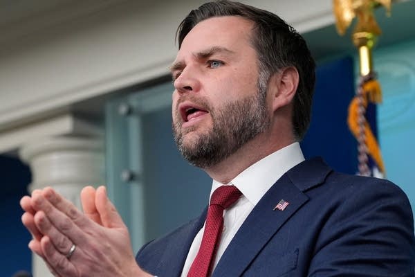 Vice President JD Vance clasps his hands while speaking at a press briefing.