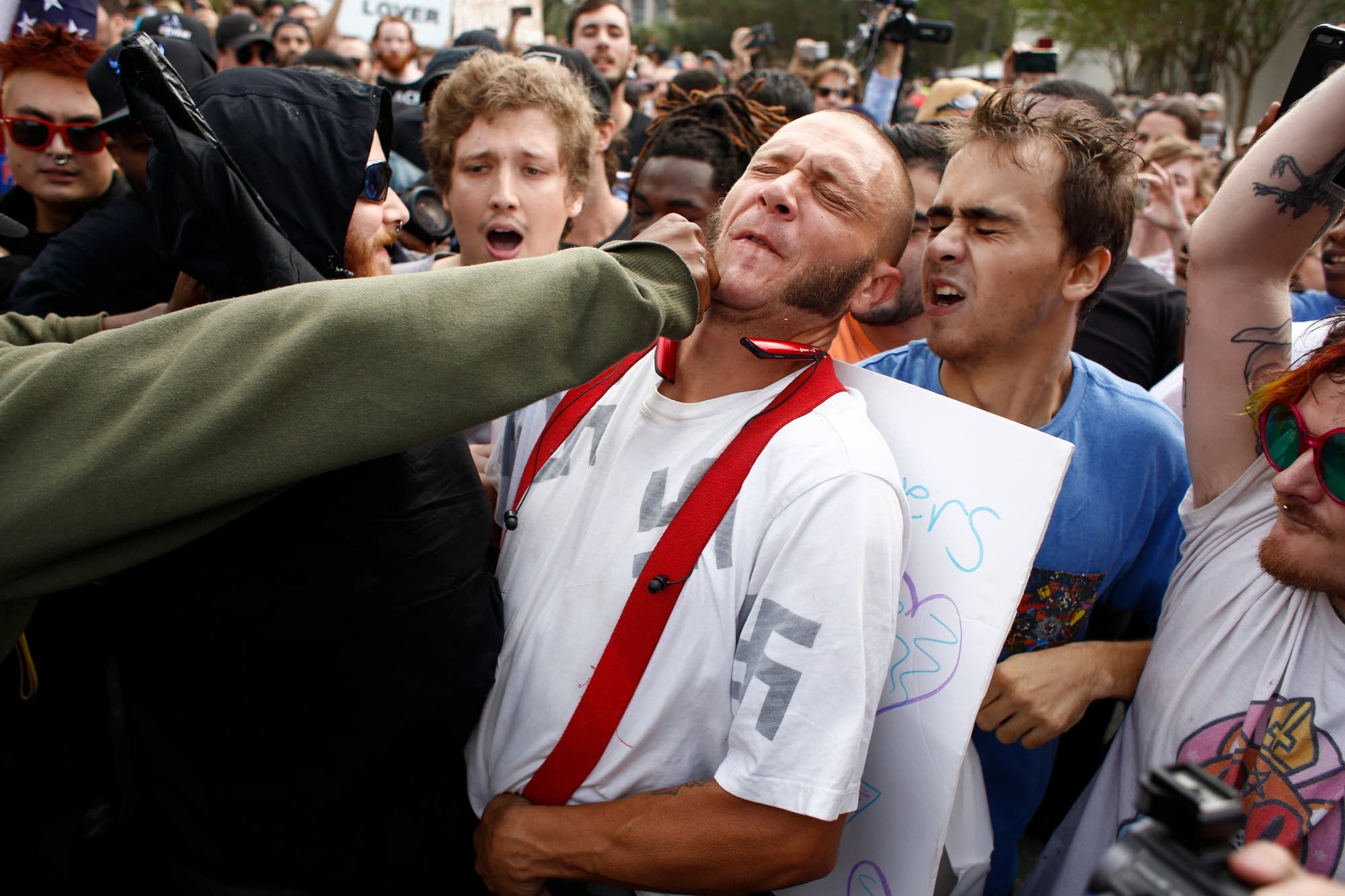 A man wearing a shirt with swastikas on it is punched.