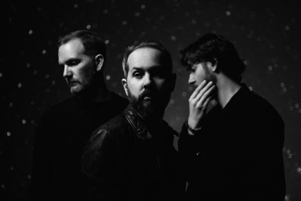 Three men, looking various directions, stand together for a group portrait