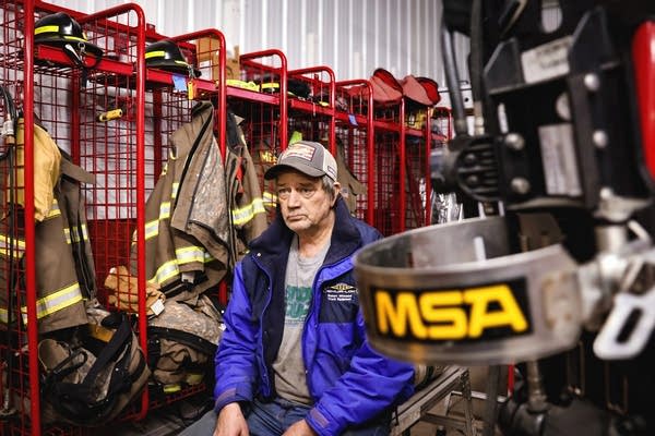 A man poses for a photo next to lockers filled with firefighter uniforms.