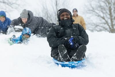 Sledders ride down a snowy hill.