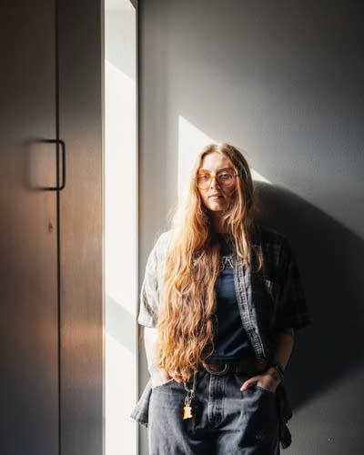 Runo Plum wears a button-down shirt over a T-shirt, jeans, and boots.
