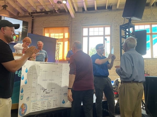 A man shows off an award in front of a tournament bracket.