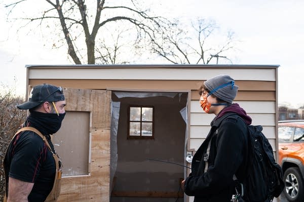 Two people stand in front of a small shed.