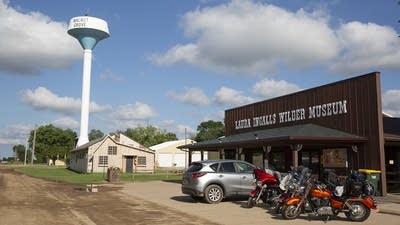 A car and motorcycles park along a dirt road in front of a wood building.