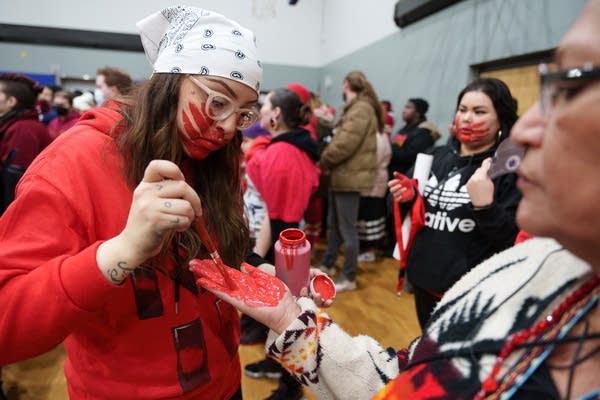 A person in red paints someones hand red for a march